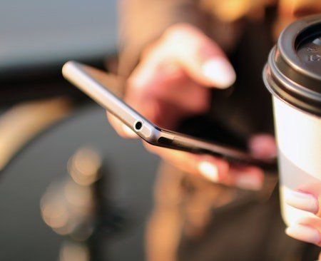 A person is holding a cup of coffee and using a cell phone.